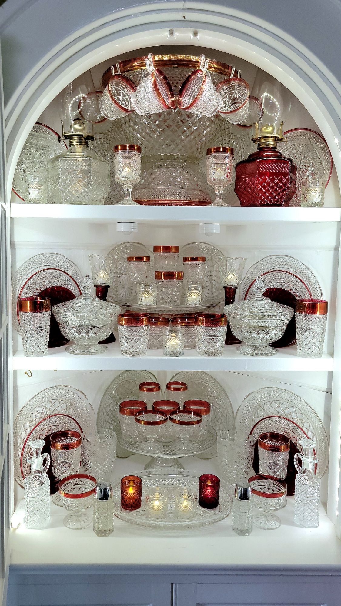 an open-doored, built-in hutch showing of it's contents of clear Wexford and ruby-banded Oxford glassware by Anchor Hocking. 