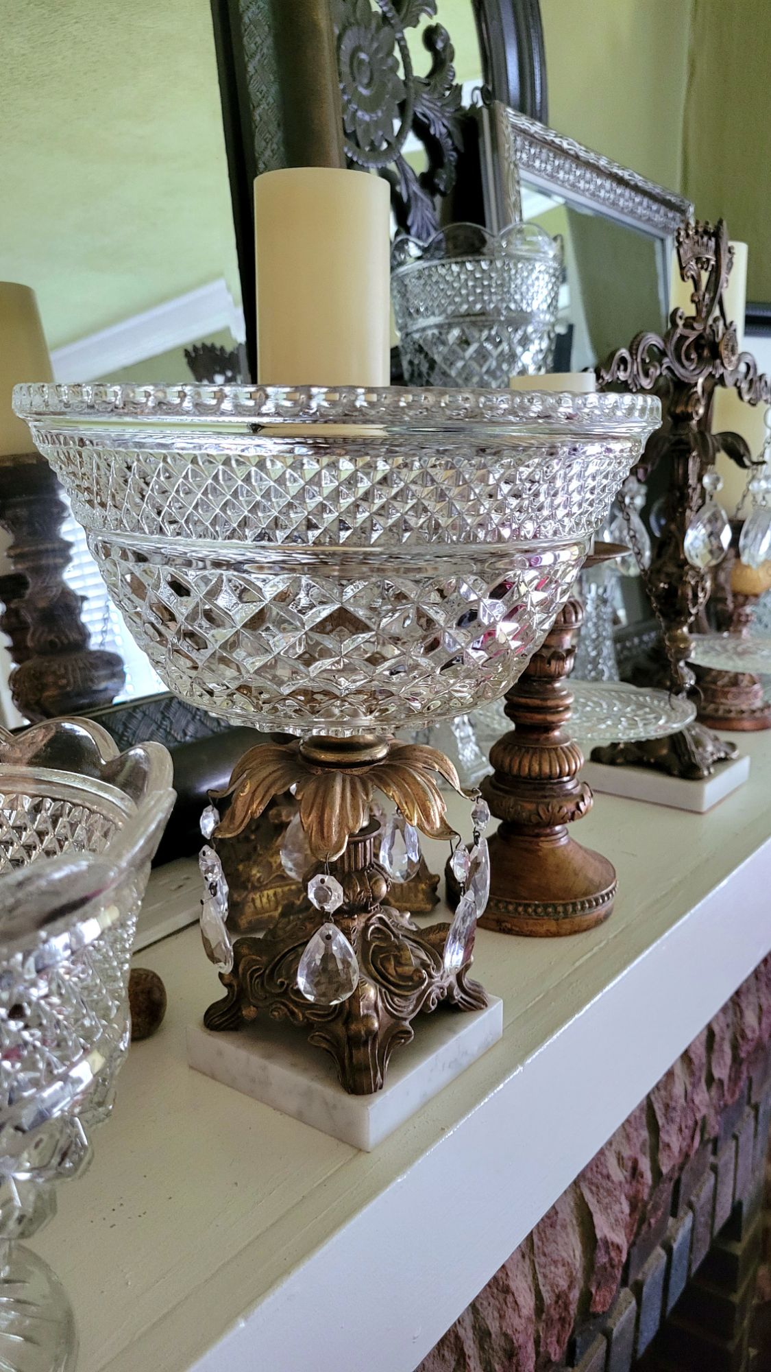a Hollywood Regency-style pedestal dish. a Wexford salad bowl/punch serves as the dish. a ring of brass scrollwork leaves drips with crystal chandelier baubles. 

the piece sits on a mantle with a collection of Wexford glassware and various gilded candlesticks. 