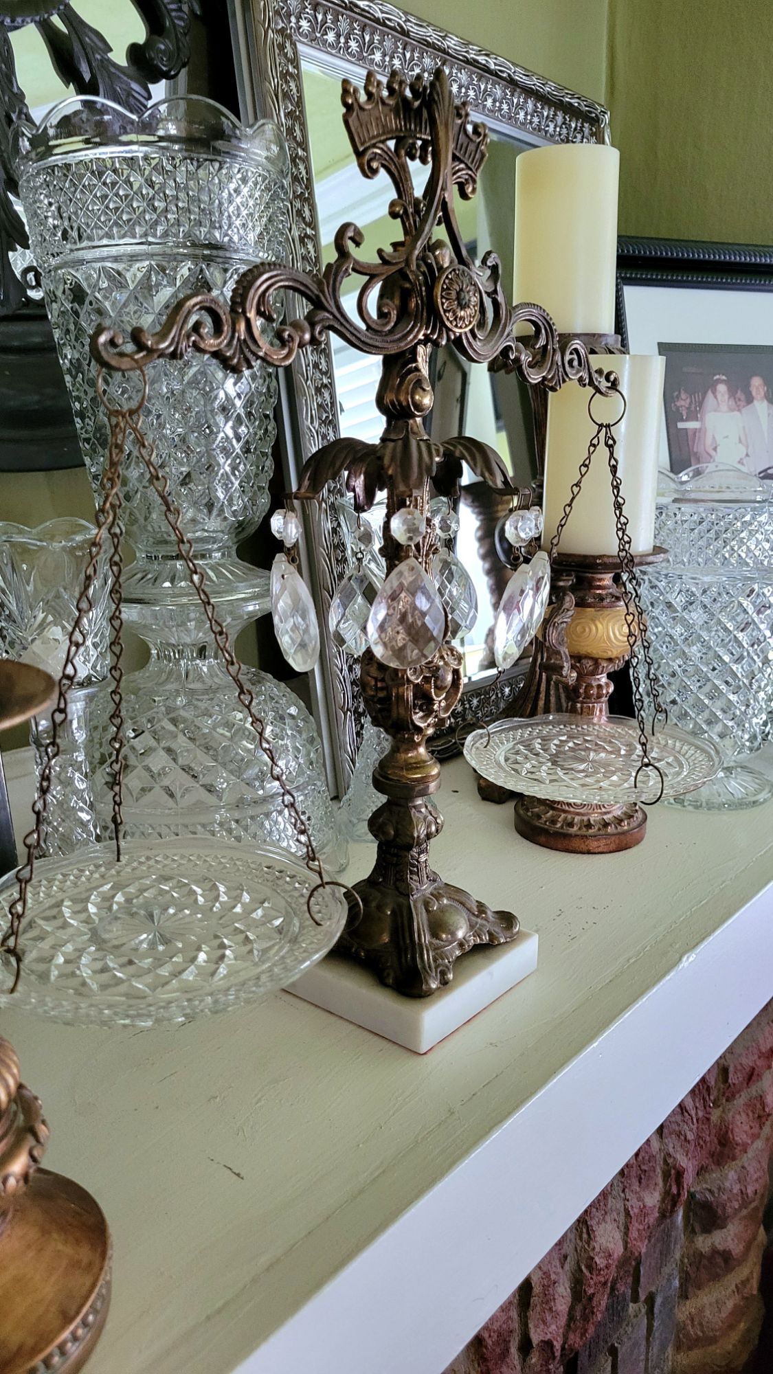 an ornate, decorative balance scale in a Hollywood Regency style. the scale pans are Wexford dessert plates by Anchor Hocking. one of the brass sections is adorned with crystal chandelier baubles.