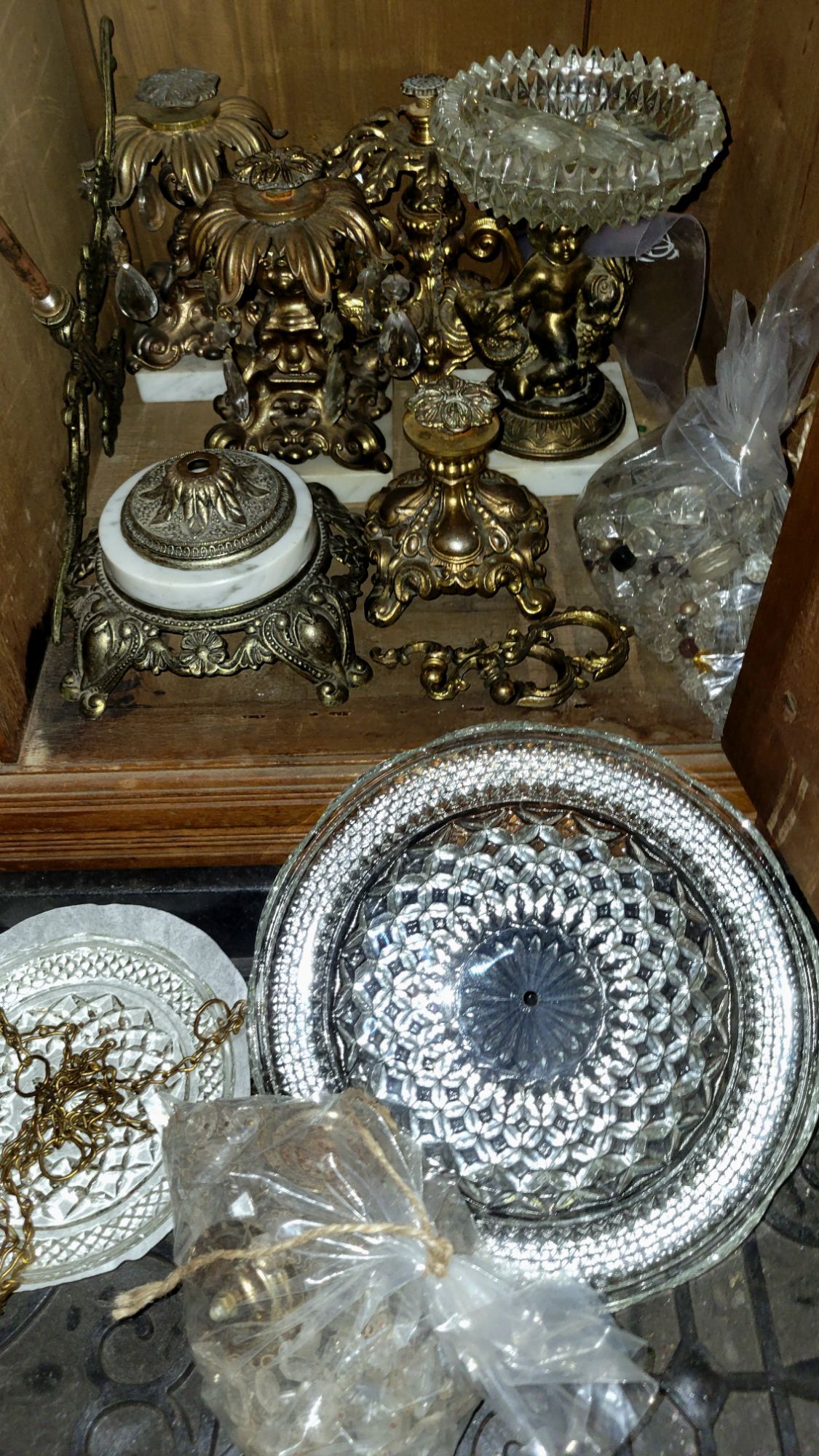 an open cabinet full of parts of Regency-style pieces, some drilled Wexford plates, and bags of glass chandelier bead-chains and baubles.