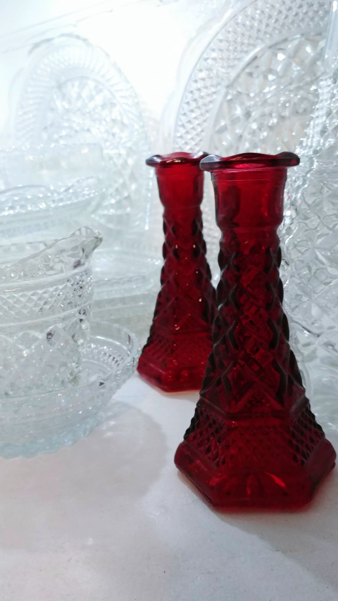 two ruby-flashed Wexford candlesticks on a white backdrop surrounded by clear Wexford glass pieces.