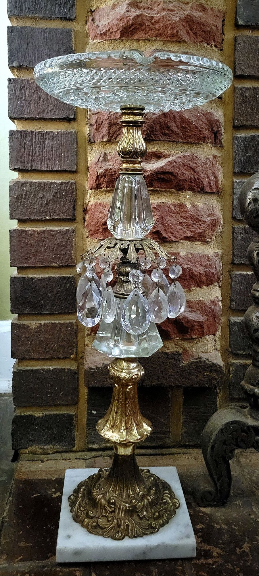 a full-length view of a Hollywood Regency style ashtray stand, featuring ornate brass fixtures, chunky glass accents, glass chandelier baubles, and a large Wexford ashtray by Anchor Hocking.