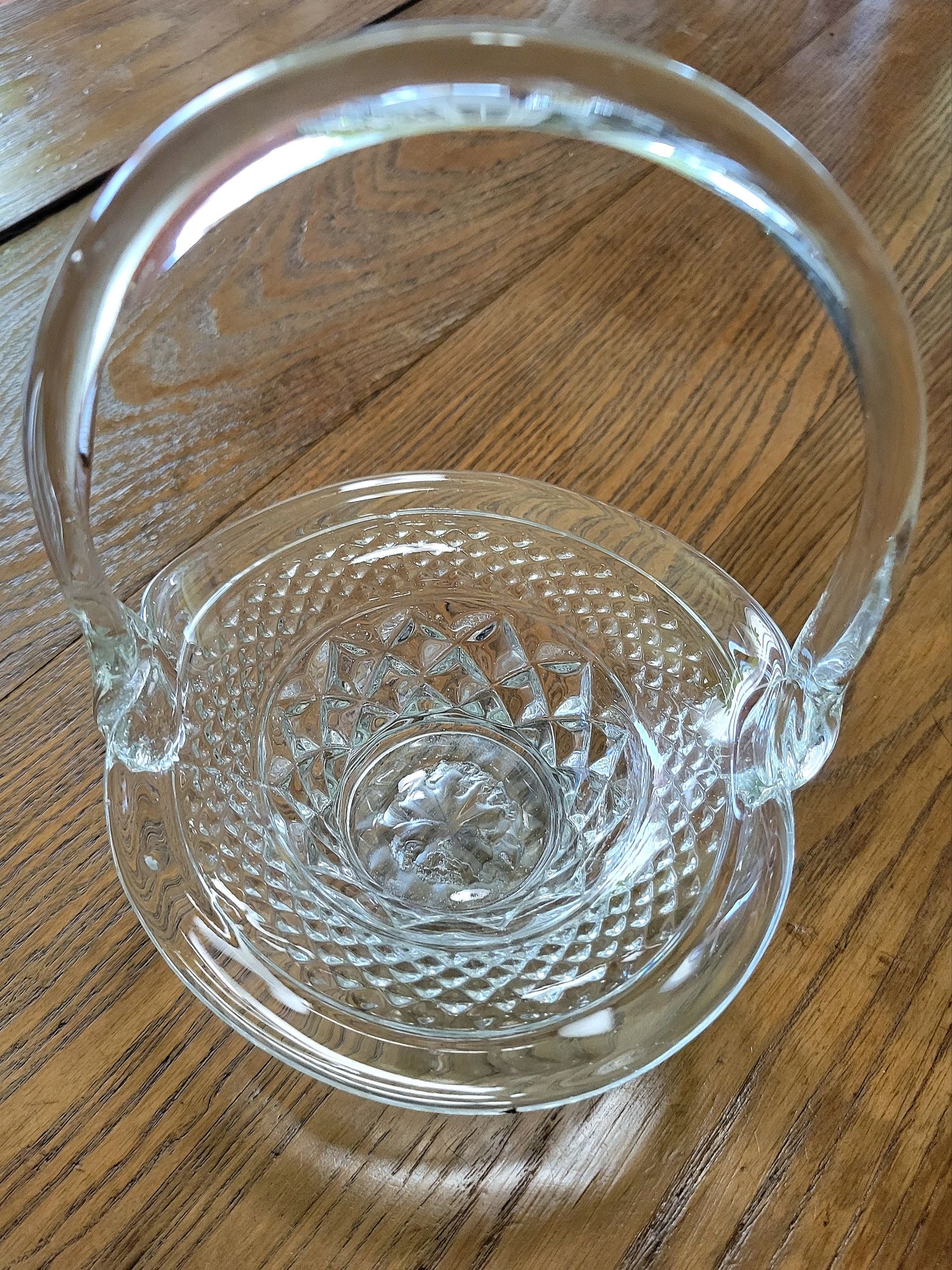 an overhead view of a pressed glass basket base, mimicking Wexford by Anchor Hocking, with a bent glass handle added presumably through a glassblowing technique.