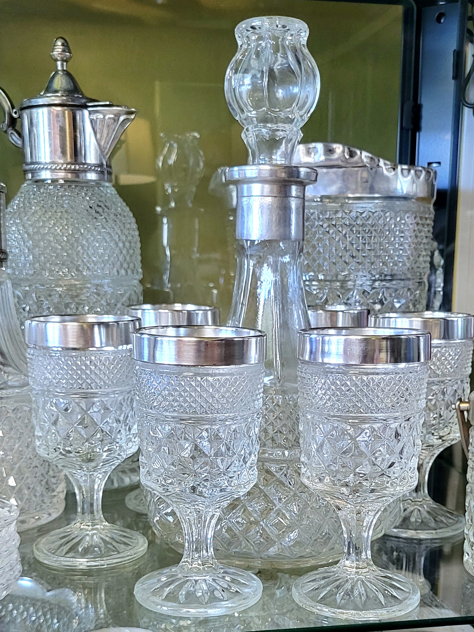 a Wexford captain's decanter, with a polished silver collar, surrounded by polished silver-trimmed wine goblets. behind the grouping is a lookalike lidded pitcher to the left, and a Wexford silver-trimmed pitcher to the right.