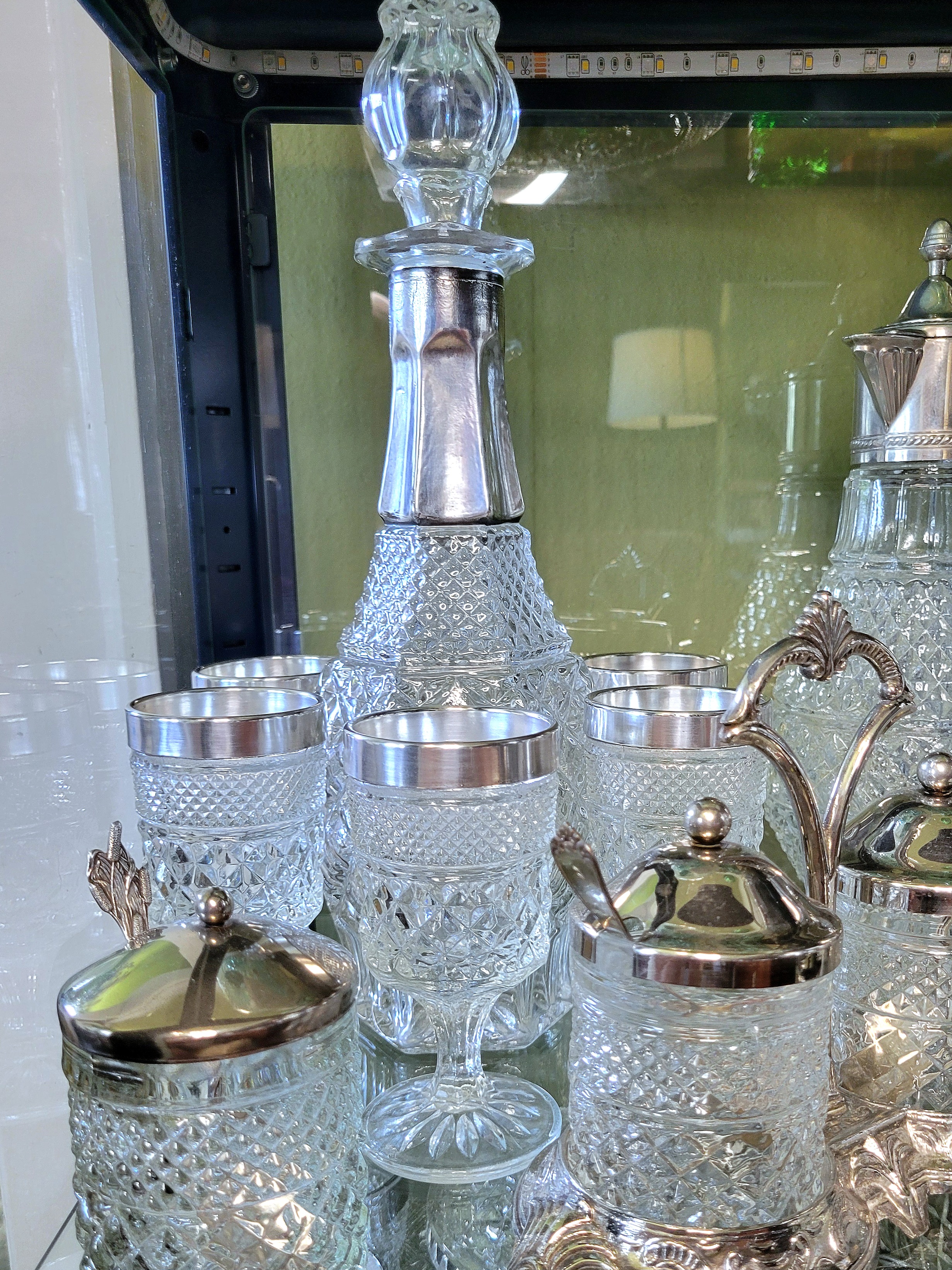 a Wexford silver-trimmed decanter set by Anchor Hocking. a wine decanter is flanked by six silver-trimmed wine goblets. lookalike pieces with silver-plated metal lids and holders surround the set.