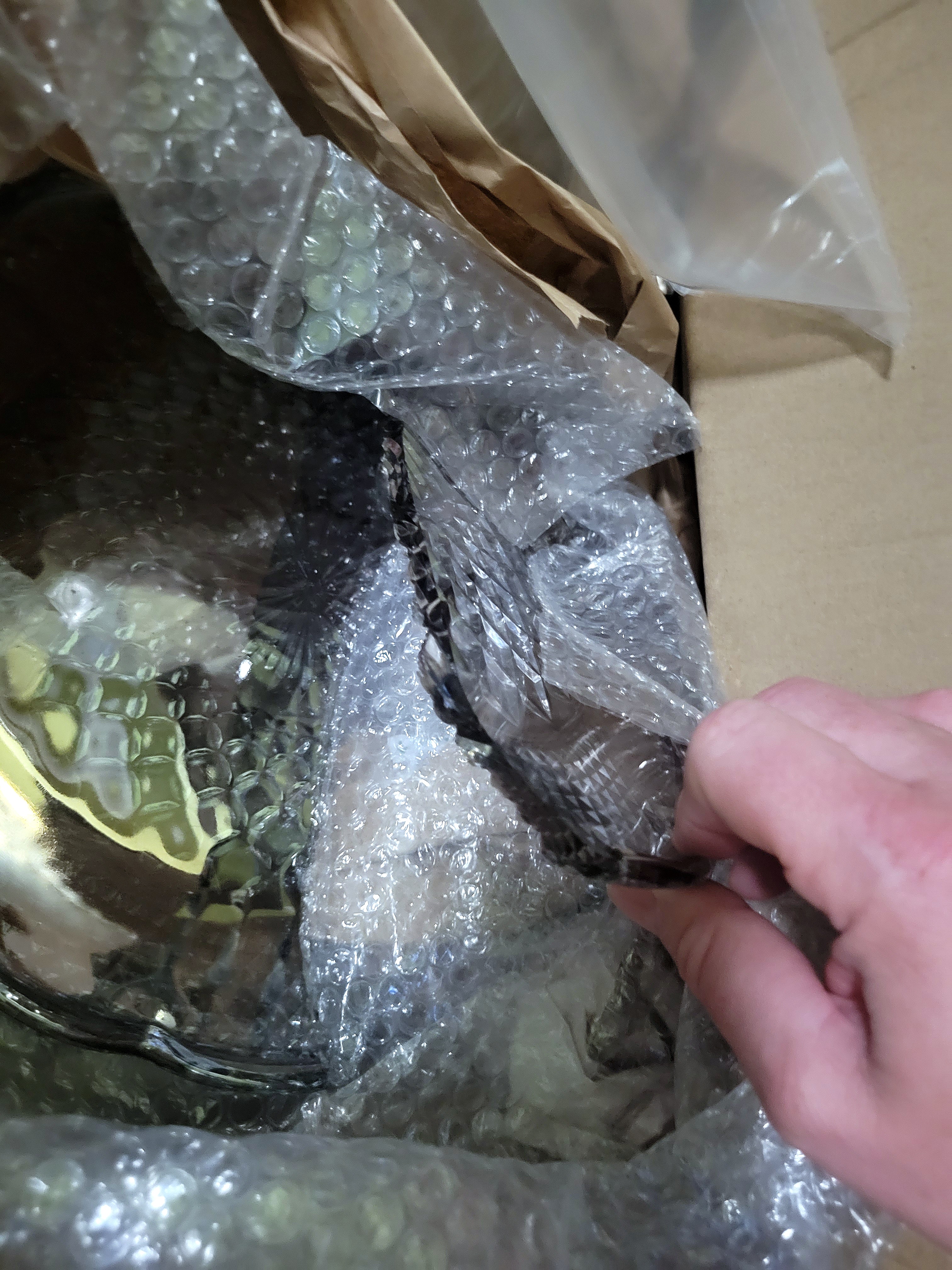 a large, dark, iridescent platter, snapped into two pieces. the pieces are framed by packing materials and the box flaps.